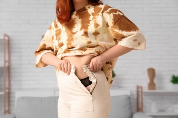 Image of woman trying to do her trousers up after pregnancy weight gain Leatherhead