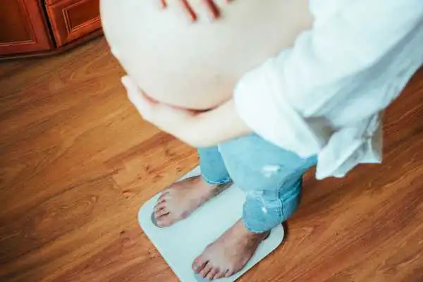Image of woman weighing herself and experiencing weight gain through pregnancy Leatherhead
